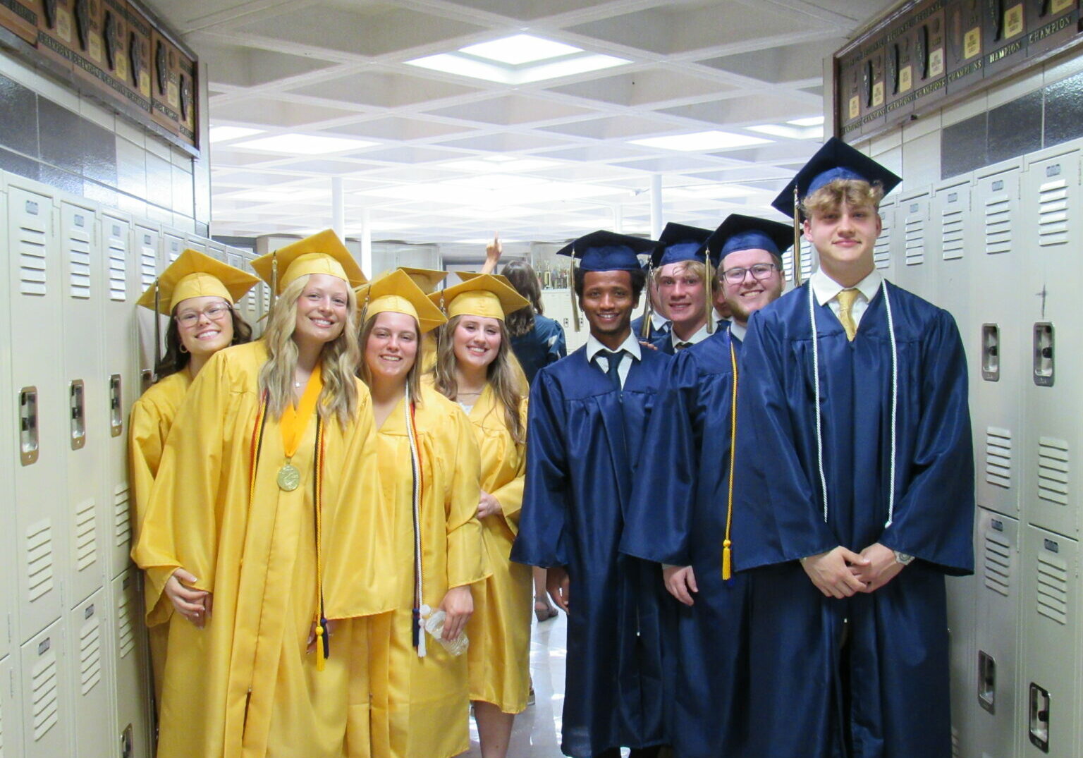 QND graduates in gold and blue caps and gowns posing in school hallway at Quincy Notre Dame High School