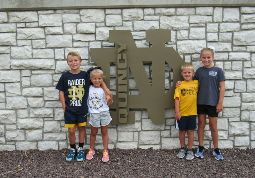 Quincy Catholic Elementary Schools - Young students standing in front of the Quincy Notre Dame High School logo, representing Raider Pride and future students